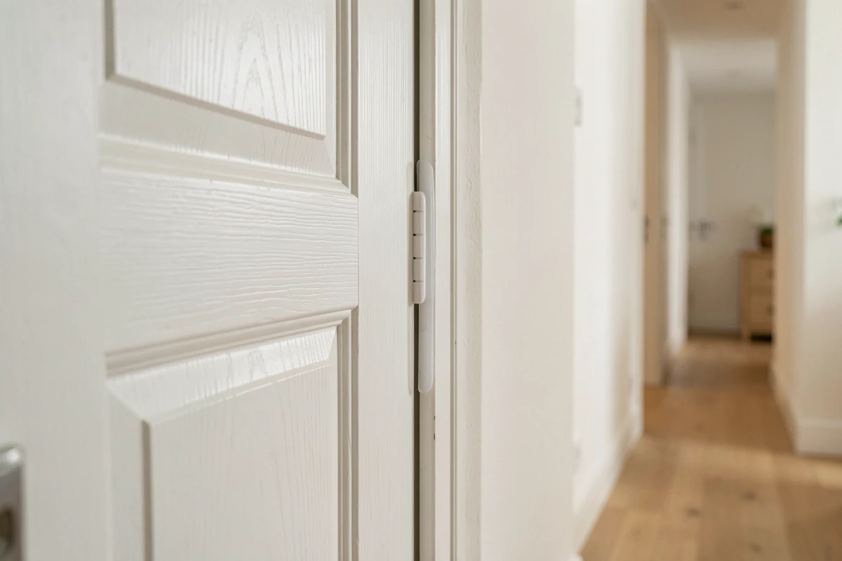 Pince doigt discrète en silicone translucide installée sur le bord charnière d'une porte intérieure blanche dans un couloir d'appartement moderne